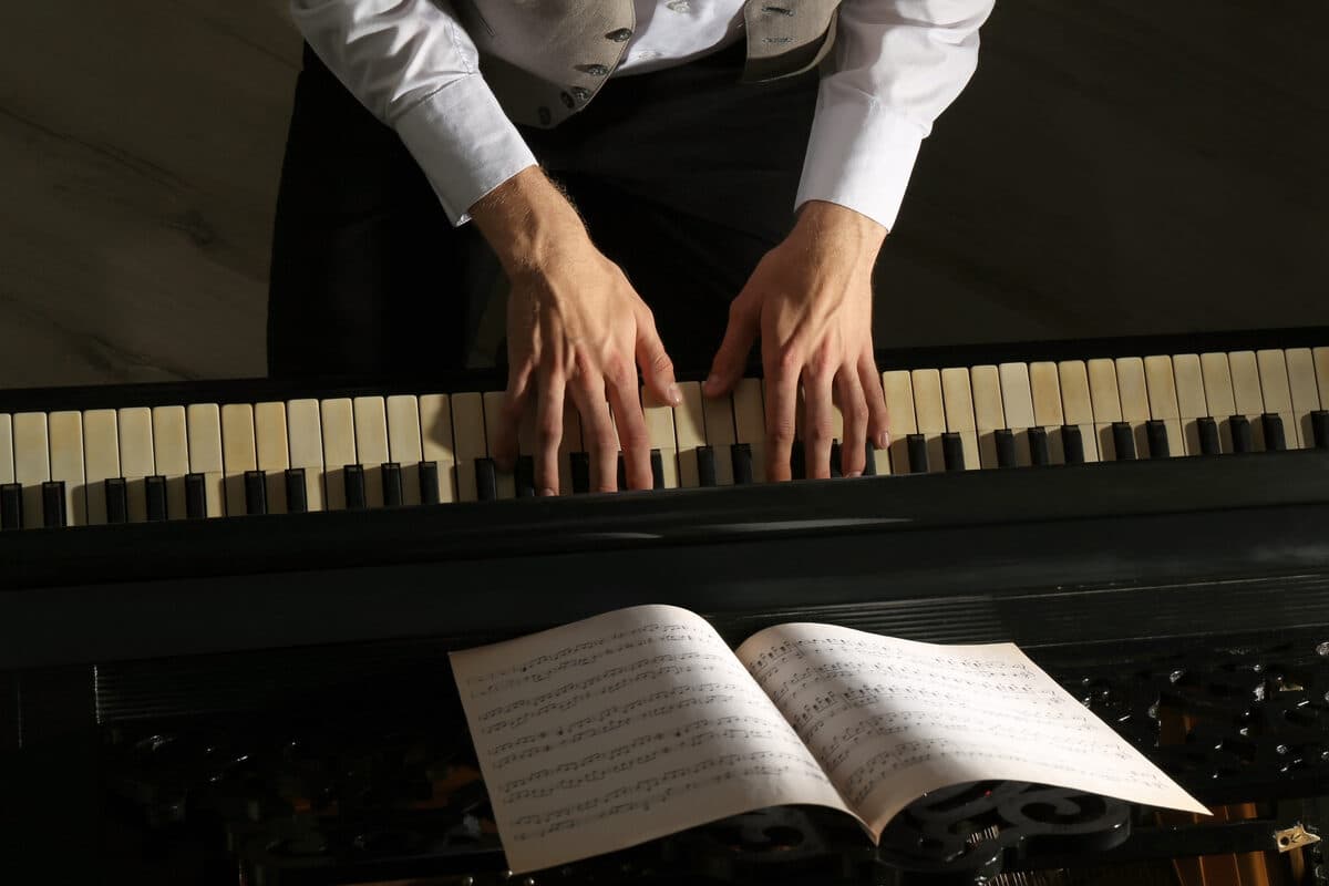 Hände eines Erwachsenen auf den Tasten eines Klaviers mit Noten – Klavier lernen als Erwachsener