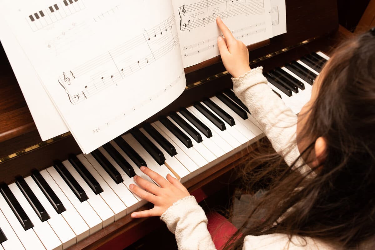 Kind lernt Klavier und zeigt auf die Noten – Klavierunterricht für Kinder